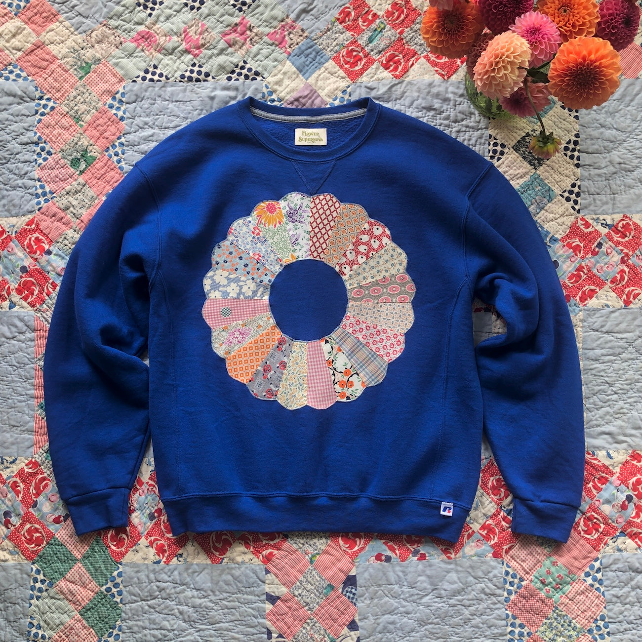 Bright blue crewneck sweatshirt with Dresden Plate vintage quilt patch sewn to front by Flower Supernova.